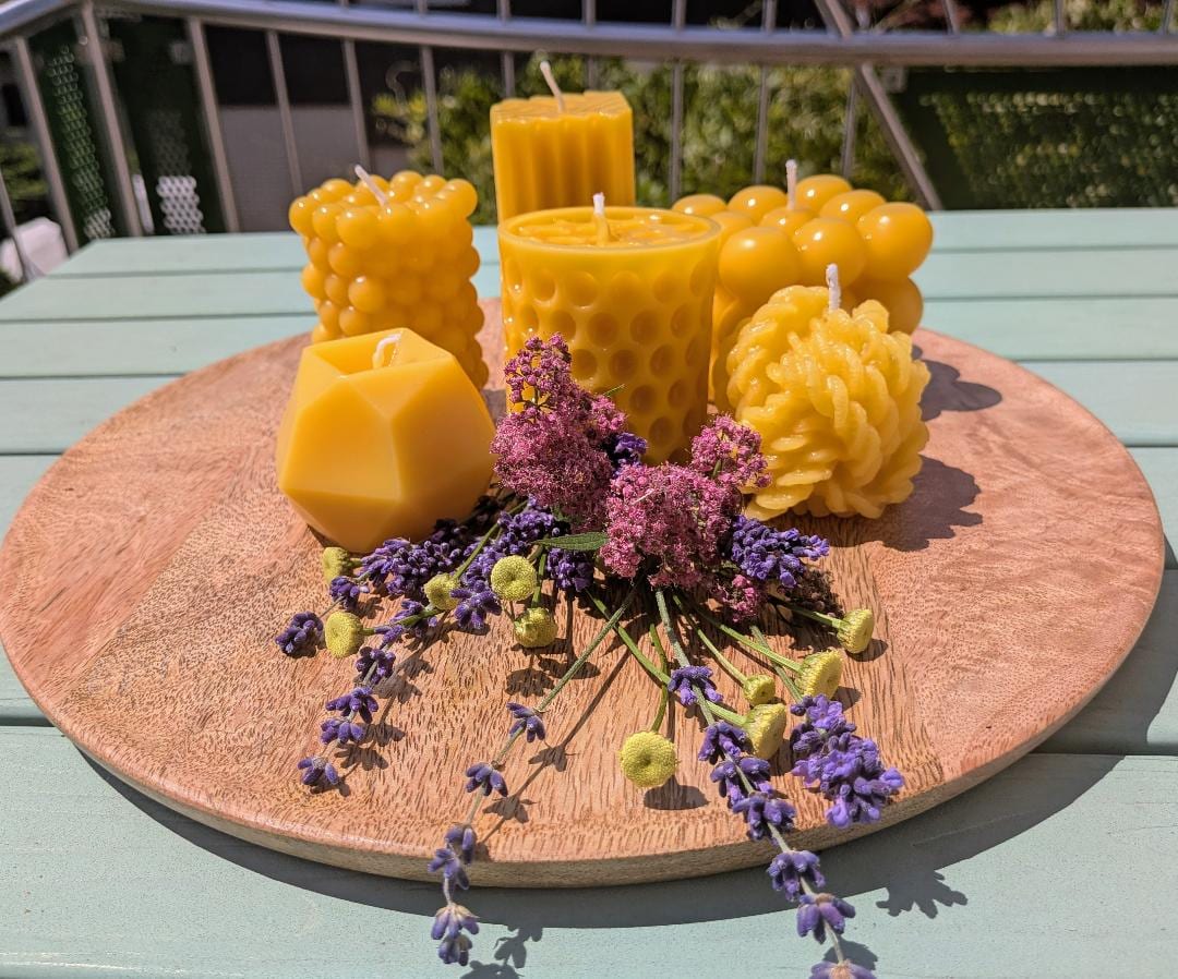 Sechs verschiedene kleine Bienenwachskerzen in unterschiedlichen Formen auf Holzscheibe mit Blumen
