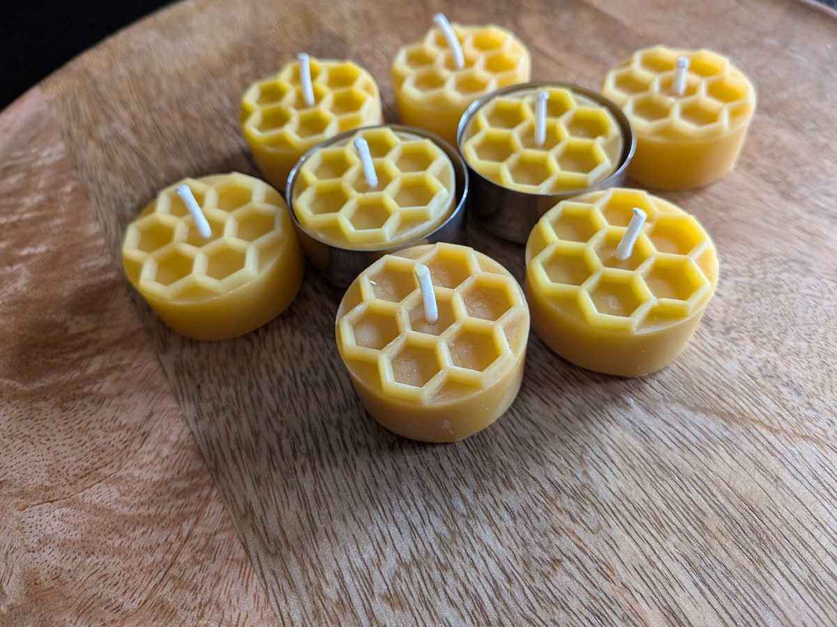 Bienenwachsteelichter mit Wabenmuster, teils in Edelstahlhüllen, auf Holzscheibe