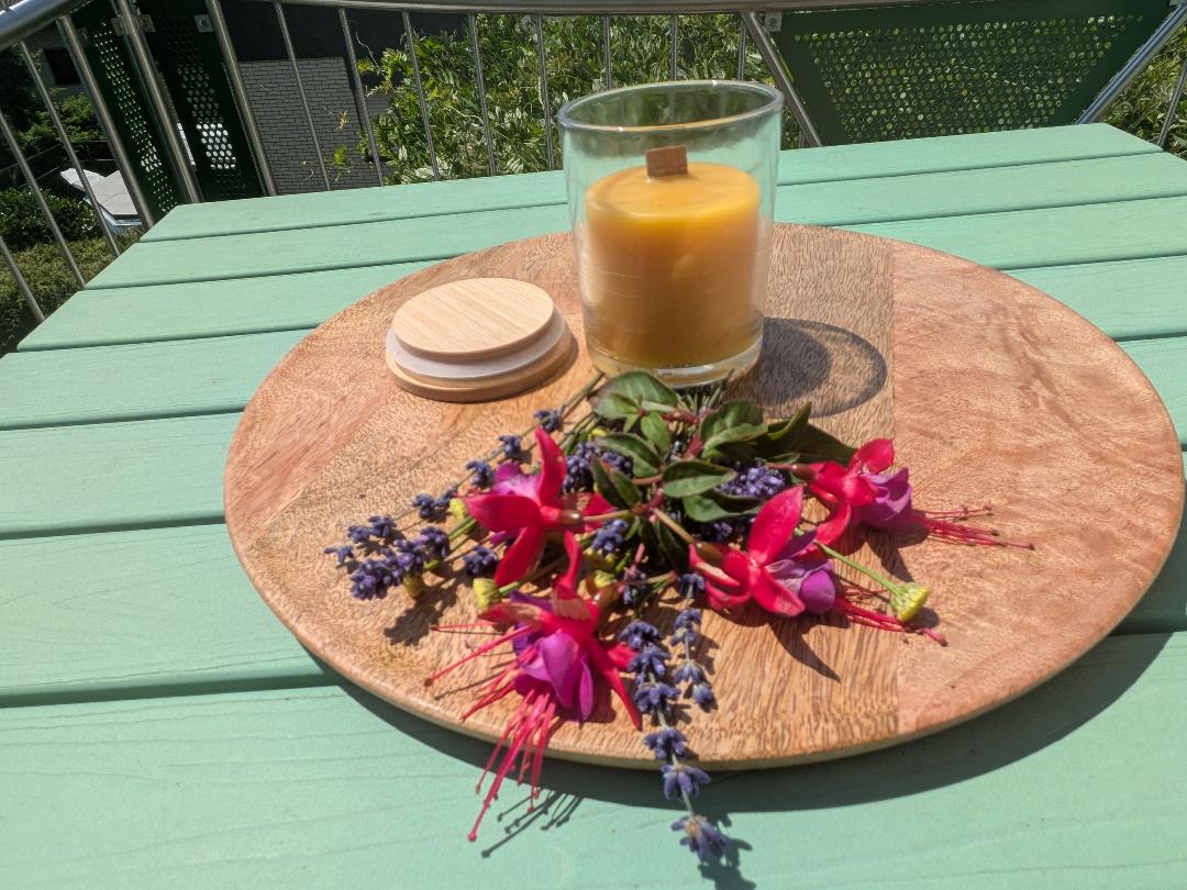 Bienenwachskerze im Glas mit Holzdocht auf Holzscheibe mit Fuchsien, Holzdeckel daneben