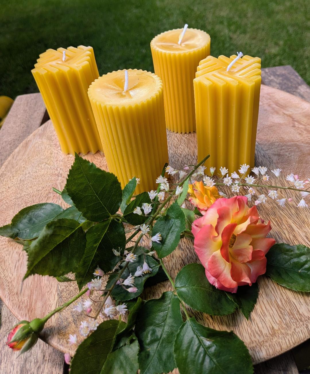 Vier quadratische Bienenwachsstumpen mit Linienmuster in zwei Formen auf Holzscheibe mit Rose