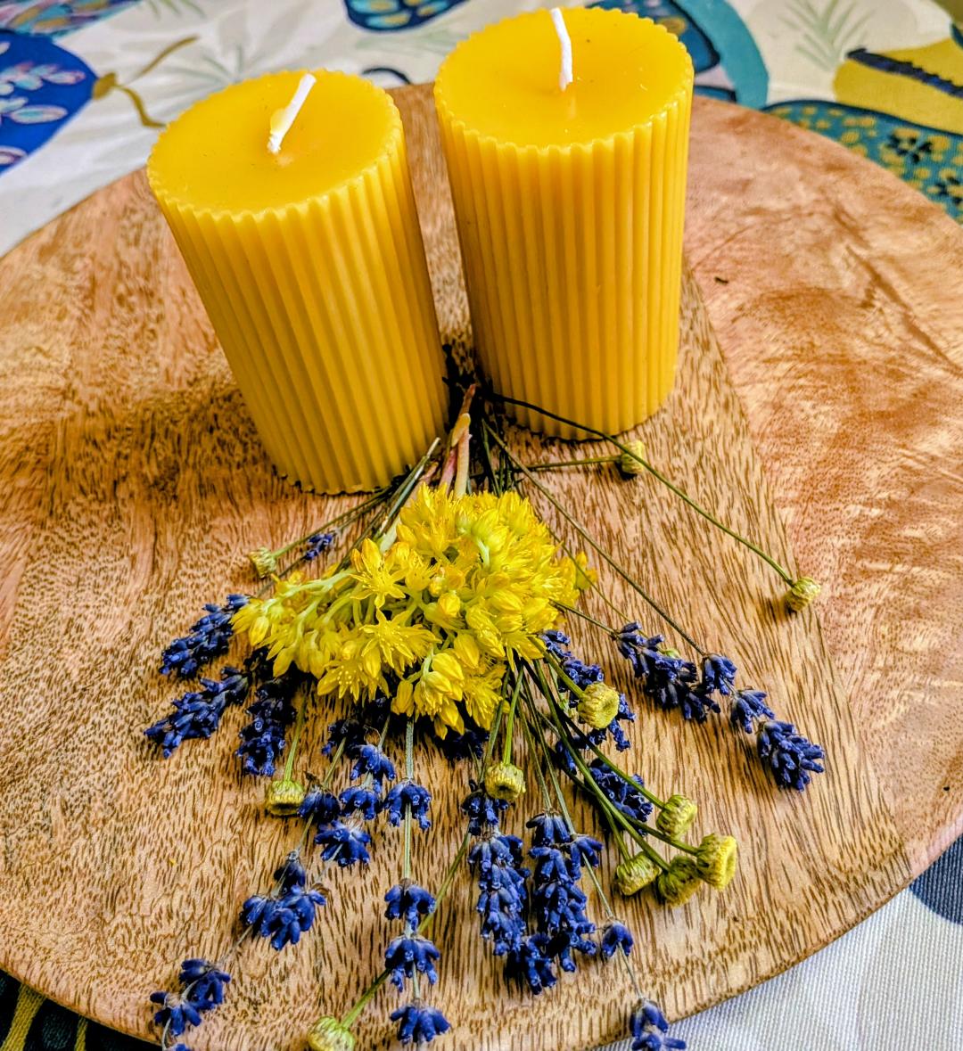 Zwei Bienenwachsstumpen mit breiten runden Rillen auf Holzscheibe mit Trockenblumen