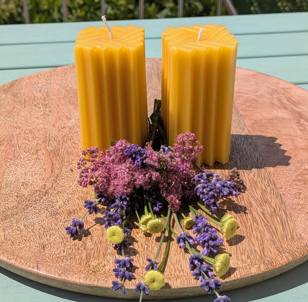 Zwei Bienenwachsstumpen mit gleichmäßigem Linienmuster auf Holzscheibe, mit Trockenblumen