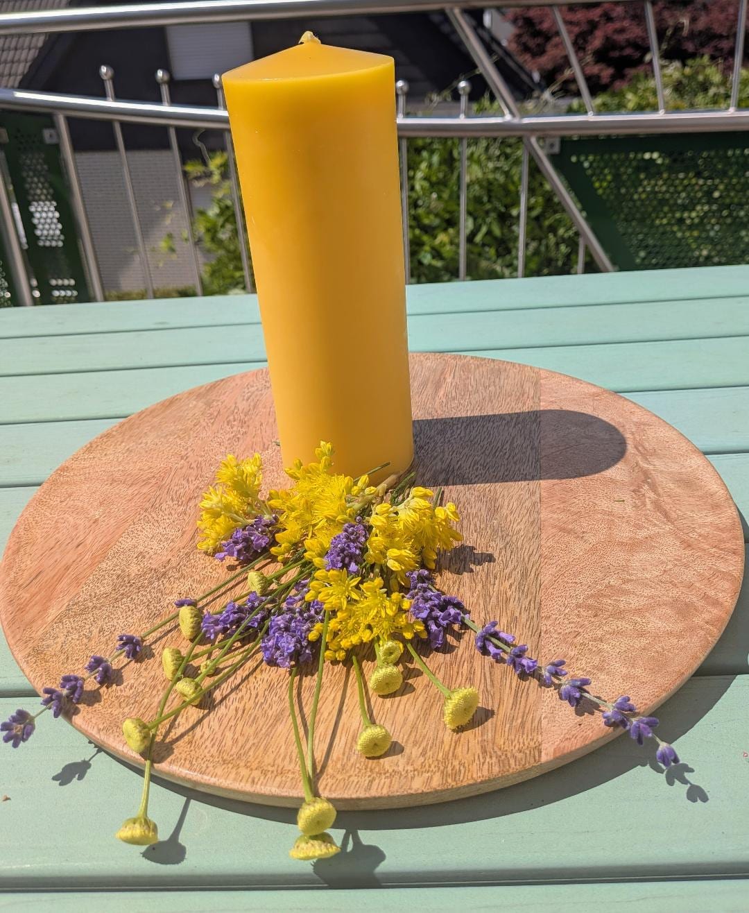 Großer schlanker Bienenwachsstumpen auf Holzscheibe, umgeben von Lavendel und Wiesenblumen